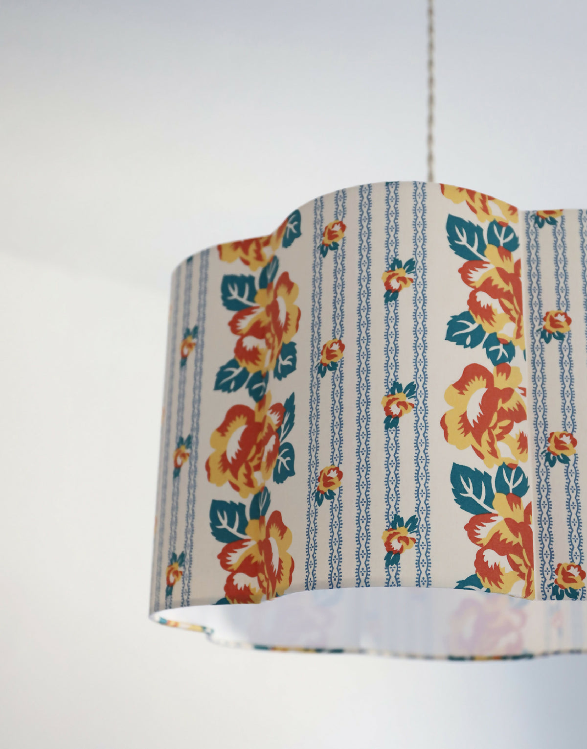 Abat-jour forme fleur en tissu bleu, fleurs orange et décor rayé de chaînettes.
