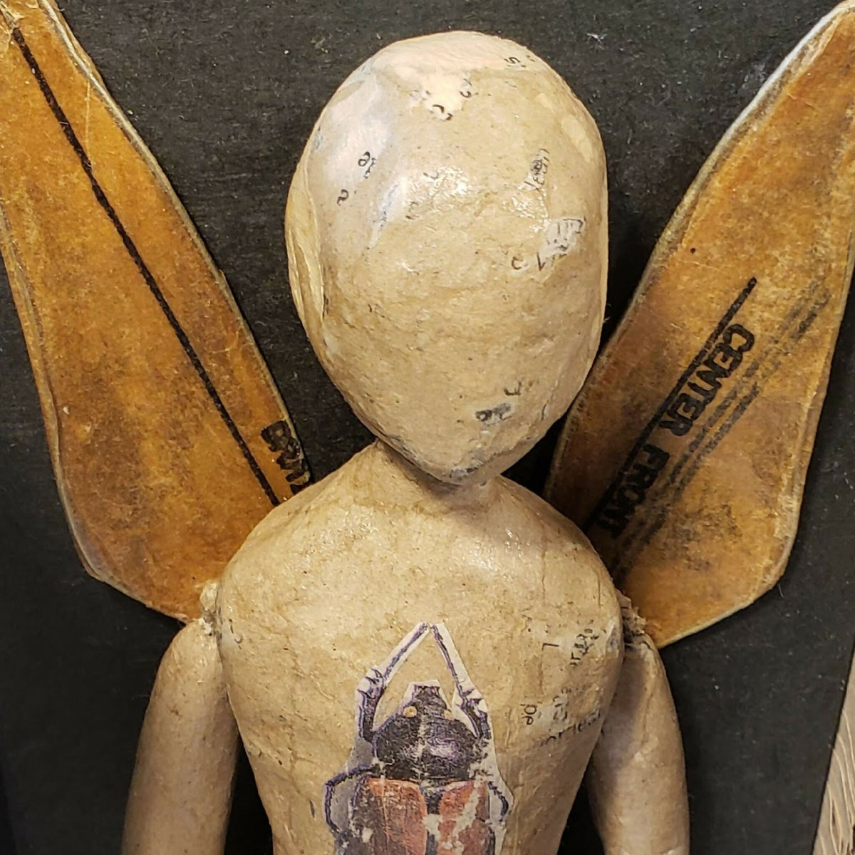 Poupée en papier beige avec ailes dorées, visage et peinture colorée sur la poitrine