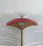 Bague de lecture en marqueterie rose posée sur un livre ouvert, vue de dessus