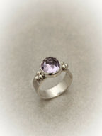 Bague en argent avec pierre améthyste ronde facettée et trois petites perles décoratives.