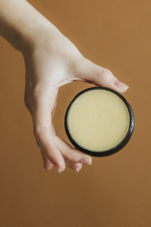 Pot de baume avec crème lisse jaune pâle, main tenant le couvercle