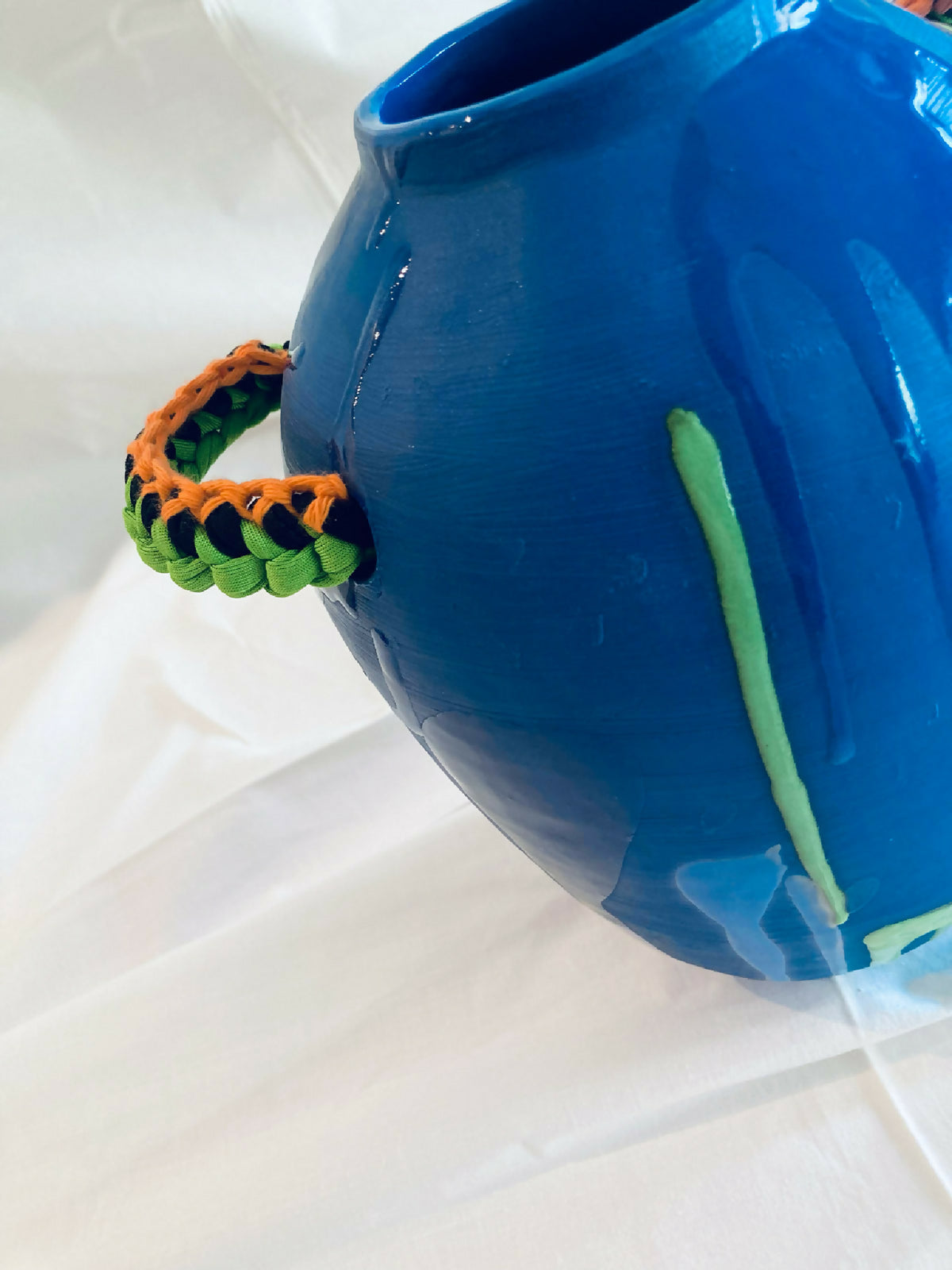 Vase amphore bleu brillant avec lanière tressée vert orange et large motif vertical vert.