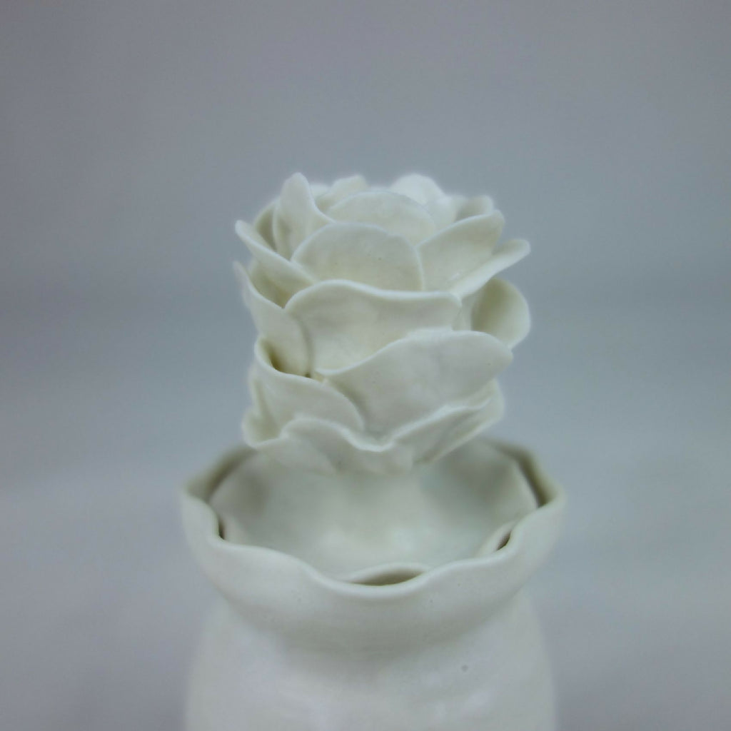 Vase en céramique blanc, gros plan des fleurs en relief au sommet.