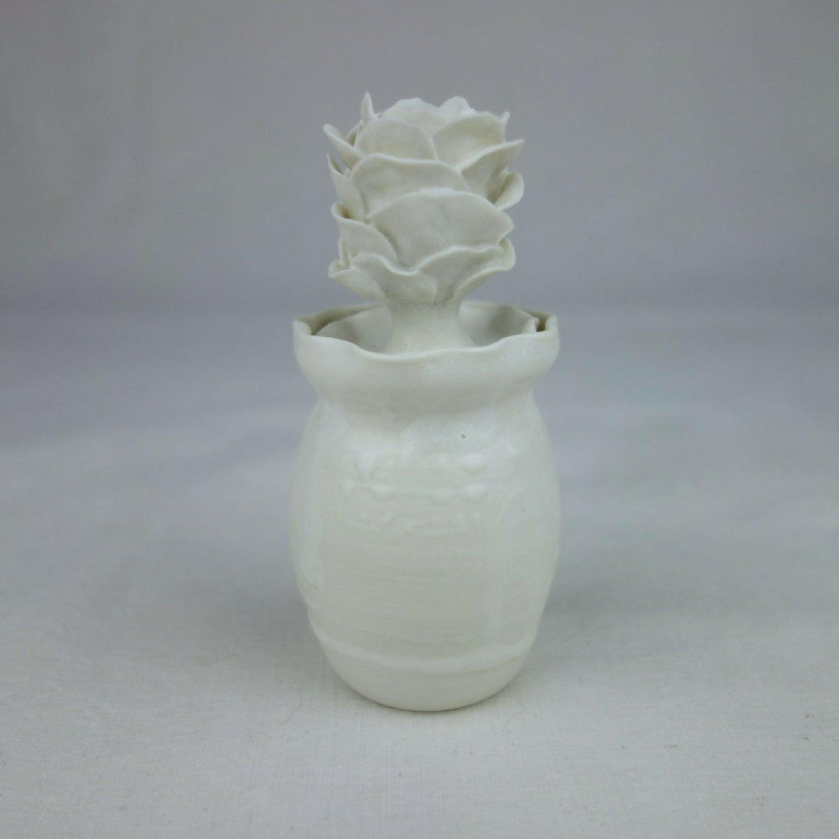 Vase en céramique blanc, forme cylindrique avec fleurs en relief sur le dessus.