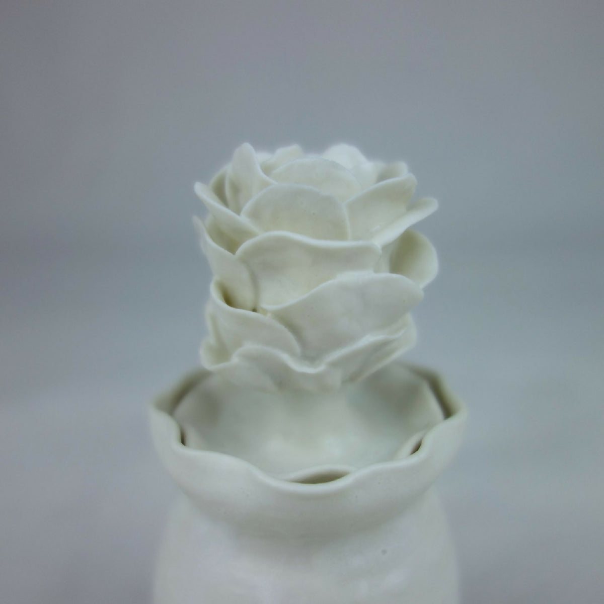 Vase en céramique blanc, gros plan des fleurs en relief au sommet.