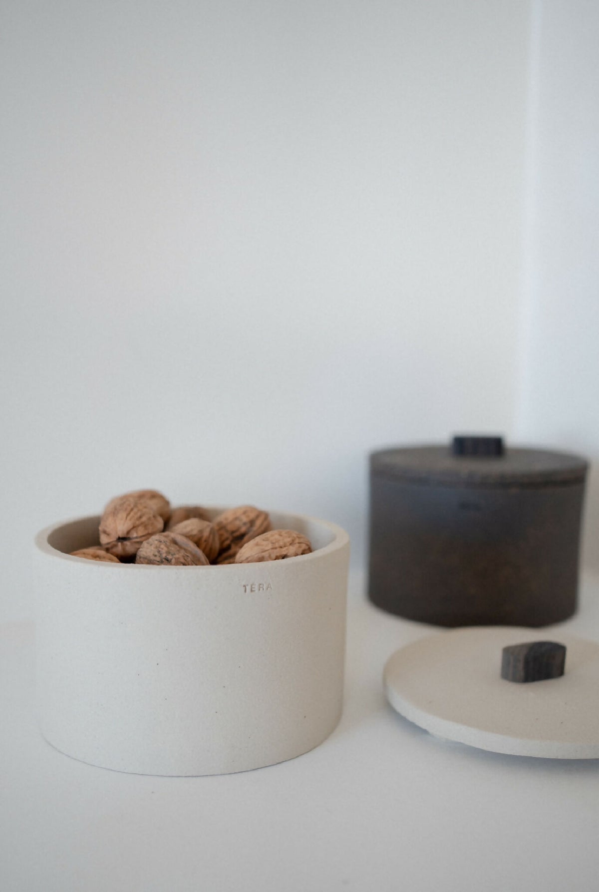 Boîte cylindrique beige TERA remplie de noix, avec couvercle noir
