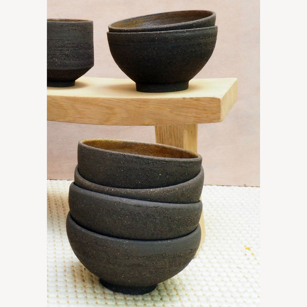 Lot de bols noirs en céramique empilés sur support en bois, finition granuleuse.