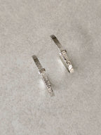 Boucles d’oreilles courbes argentées avec détails texturés, fermoirs visibles