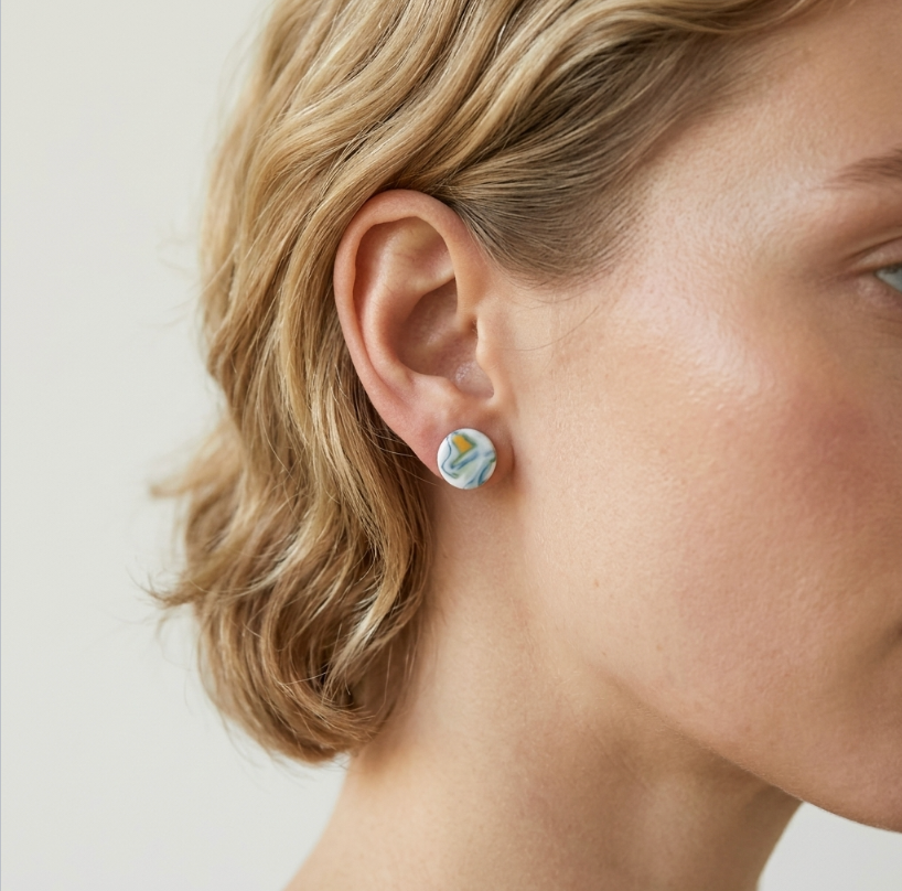 Boucles d’oreilles clous en porcelaine marbrée blanc, bleu, jaune et vert, sur l’oreille