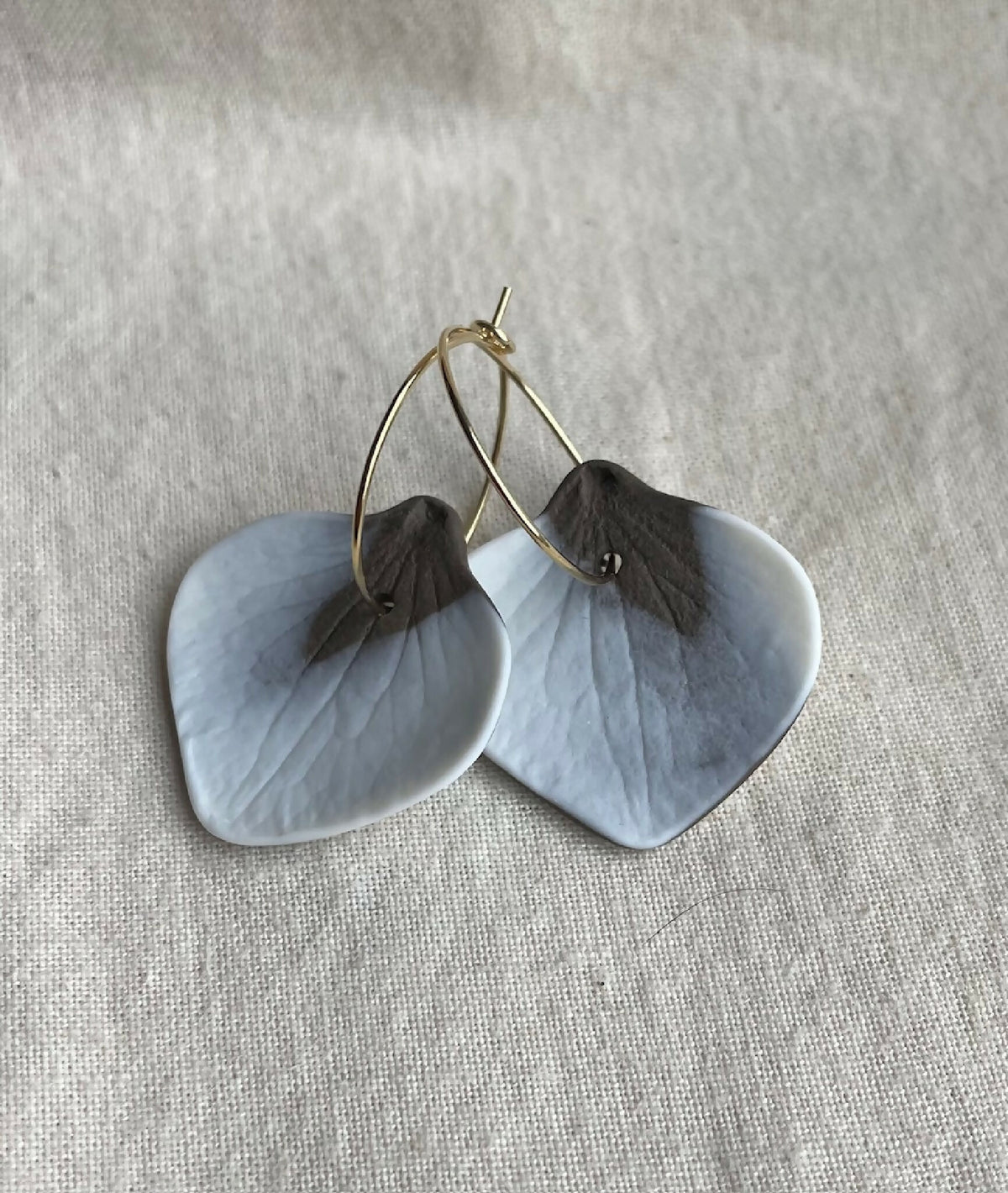 Boucles d’oreille créoles en porcelaine, pétales bleu ciel et détails sombres.