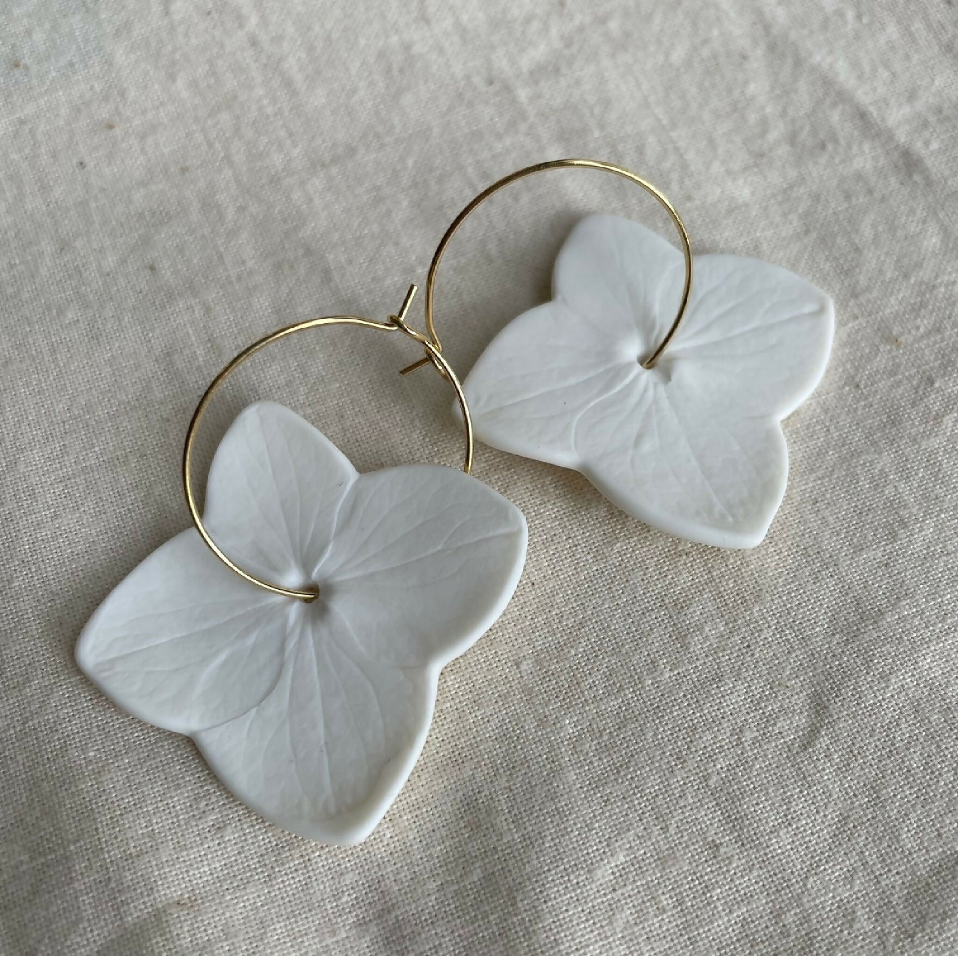 Boucles d’oreilles créoles avec fleurs en porcelaine blanche et montures dorées.