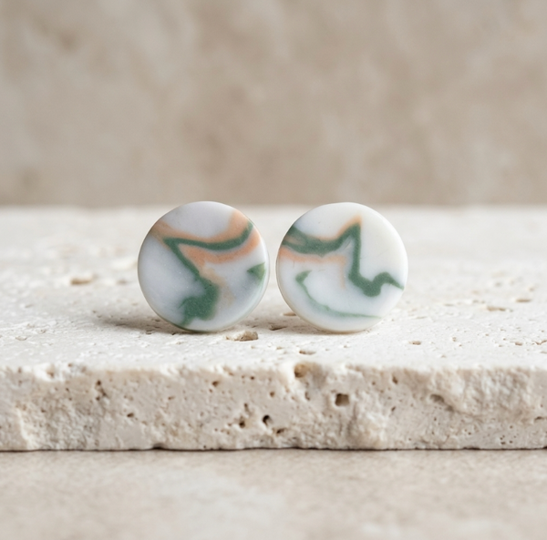 Paire de clous d’oreille ronds en porcelaine blanche, motifs marbrés verts sur fond clair.