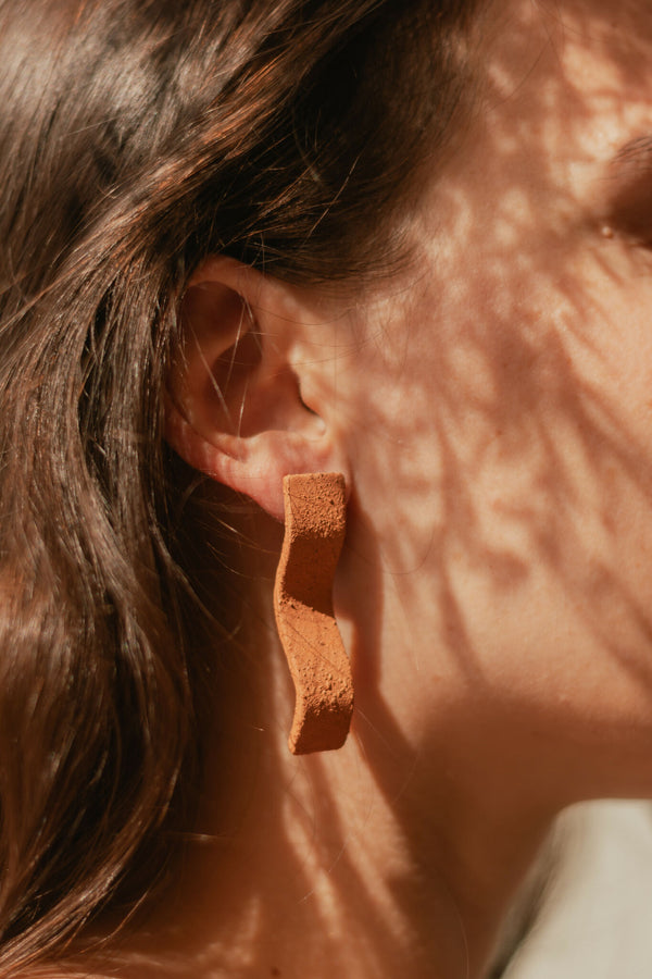 Boucles d’oreilles pendantes en barres courbées couleur terre cuite, gros plan à l’oreille