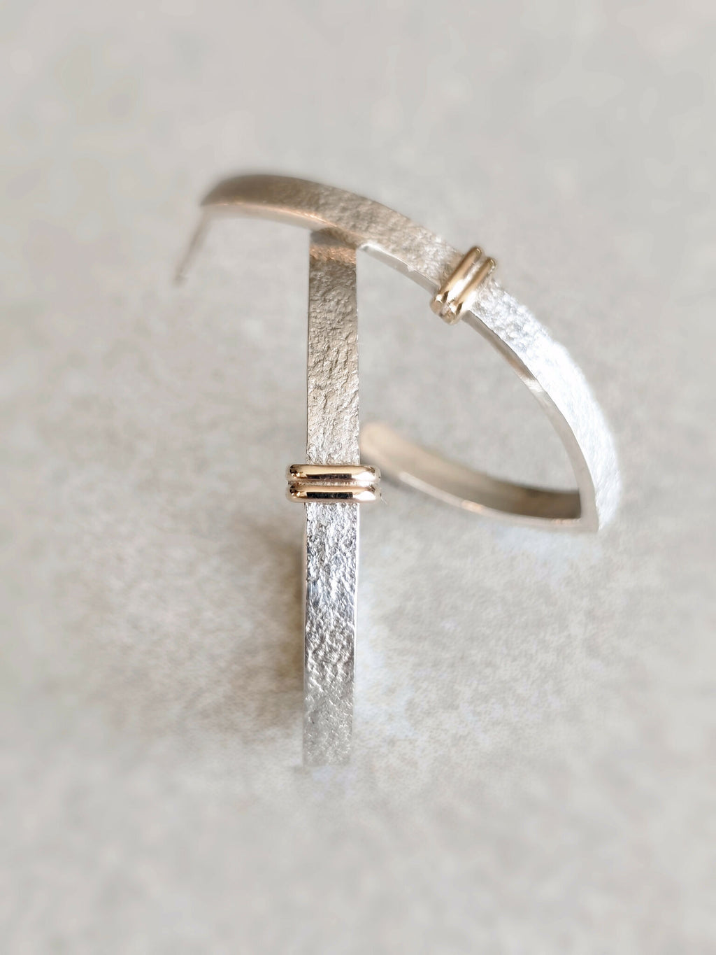 Boucle d’oreille courbe argentée texturée avec fermoir doré, vue rapprochée