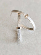 Boucle d’oreille courbe argentée texturée avec fermoir doré, vue rapprochée