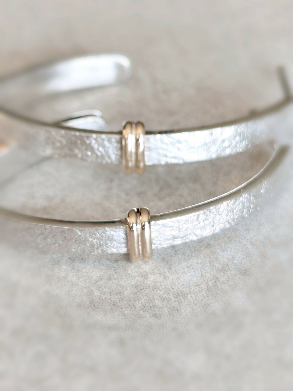 Détails des boucles d’oreilles courbes argentées : fermoirs dorés et surface texturée