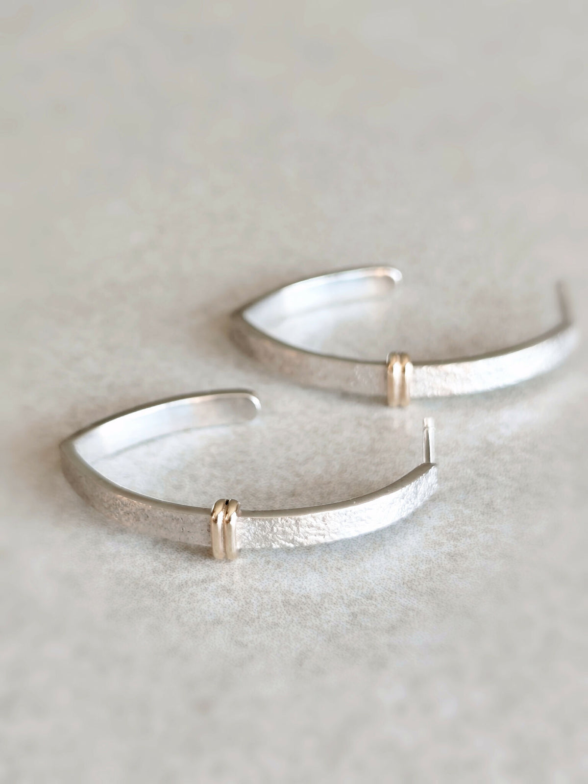Boucles d’oreilles courbes argentées brillantes avec anneaux dorés sur la jonction
