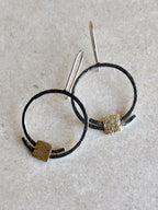 Boucles d’oreilles pendantes en anneaux : deux anneaux noirs avec carrés dorés texturés, tiges fines.