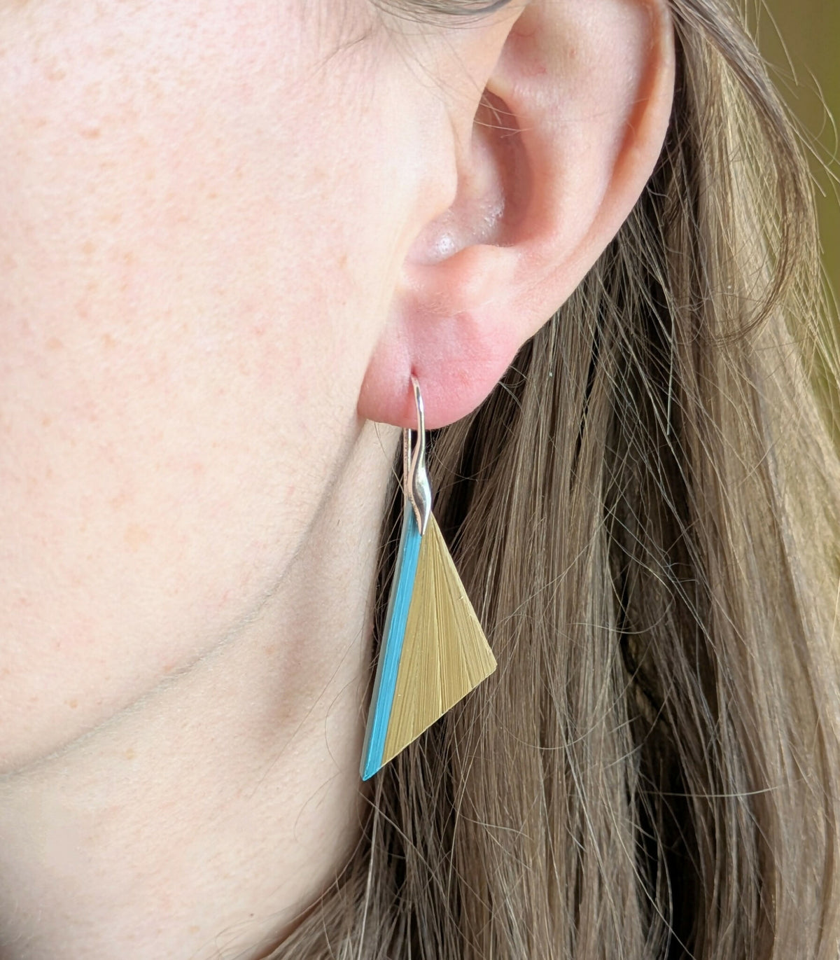 Boucles d’oreilles triangulaires paille dorée et turquoise, sur crochets argent, portées.