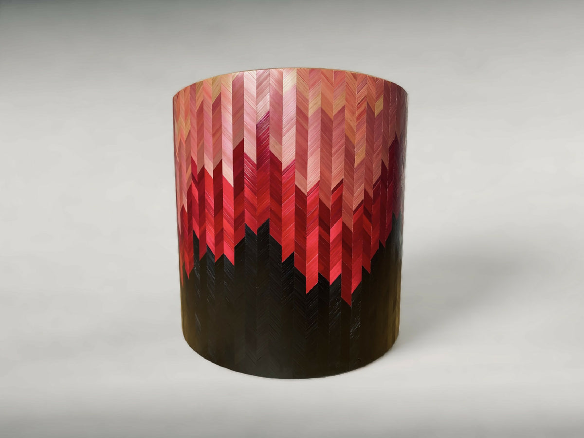 Bout de canapé rond à motif chevrons rouge, rose et beige, base sombre.