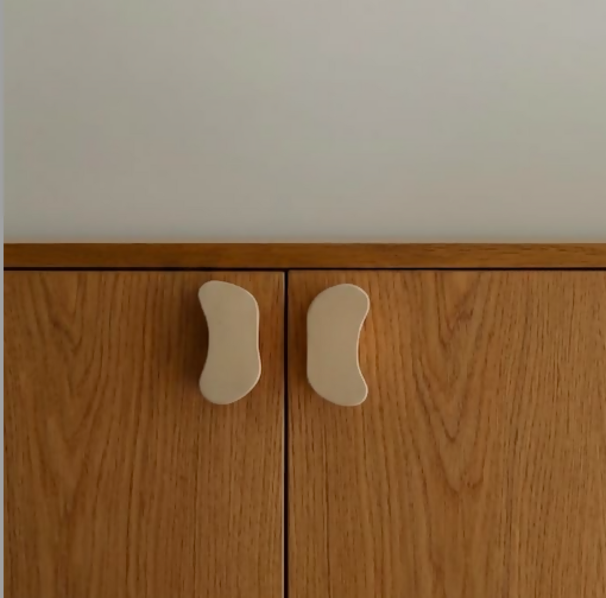 Boutons de porte Halo gris clair, boutons ovales asymétriques sur panneau en bois.