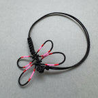 Bracelet noir en cordon tressé avec libellule rose et rouge, nœud central visible.