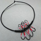 Bracelet noir en cordon tressé avec libellule rose et rouge, nœud et brins visibles.