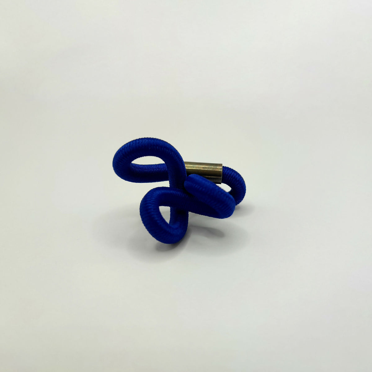 Broche en entrelacs de tissu bleu et tige métallique dorée.