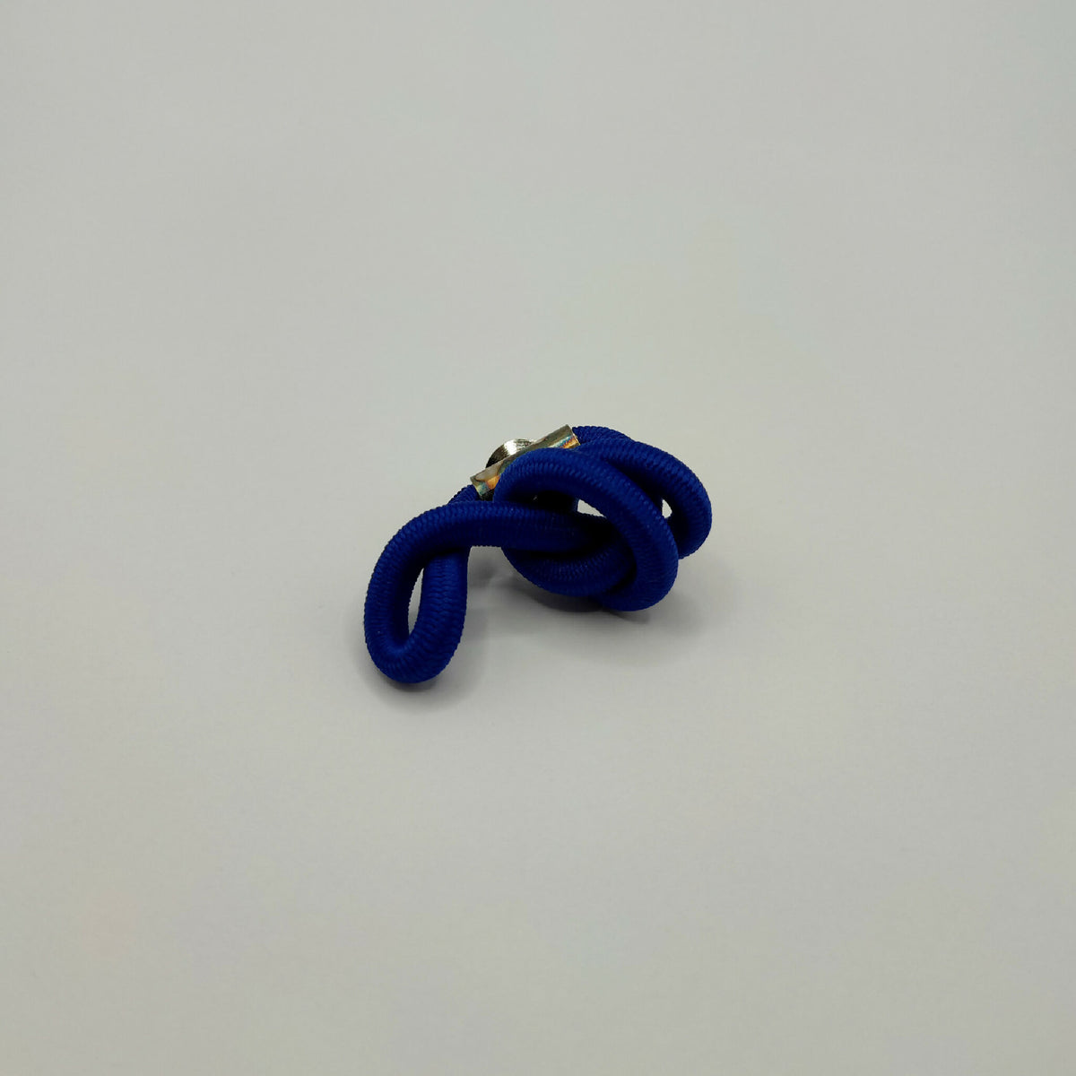 Broche en tissu bleu entrelacé, épingle métal doré visible.