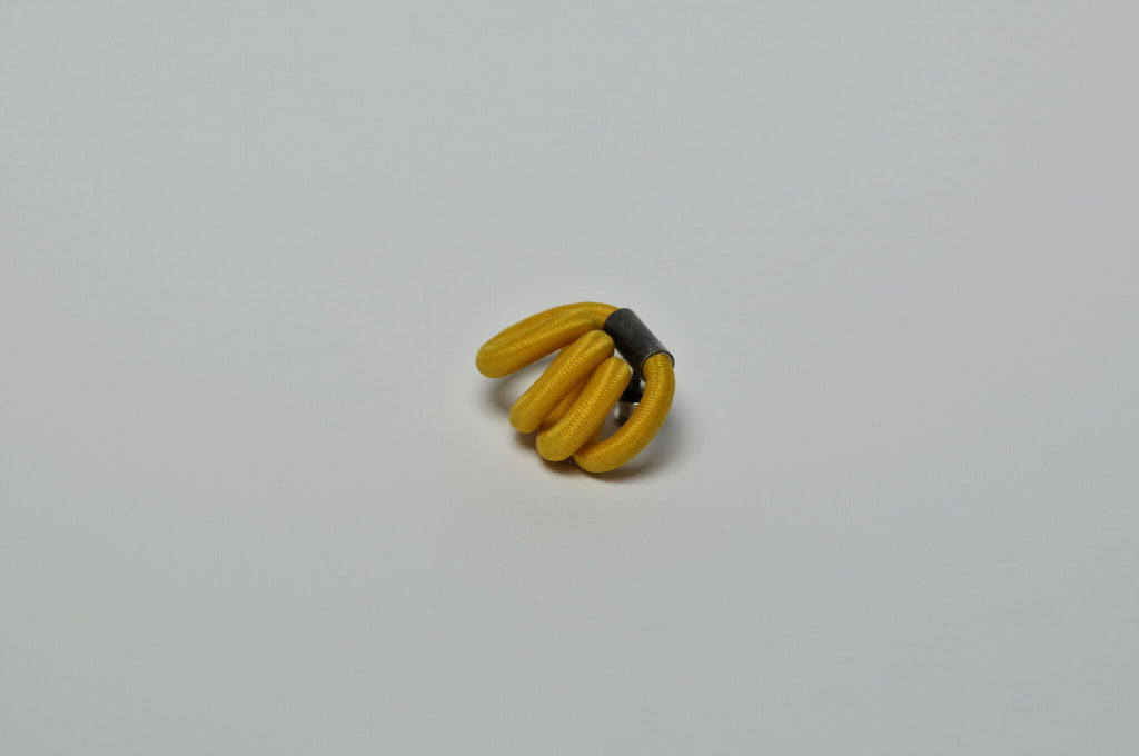 Broche entrelacée jaune, fermoir noir visible, vue rapprochée.
