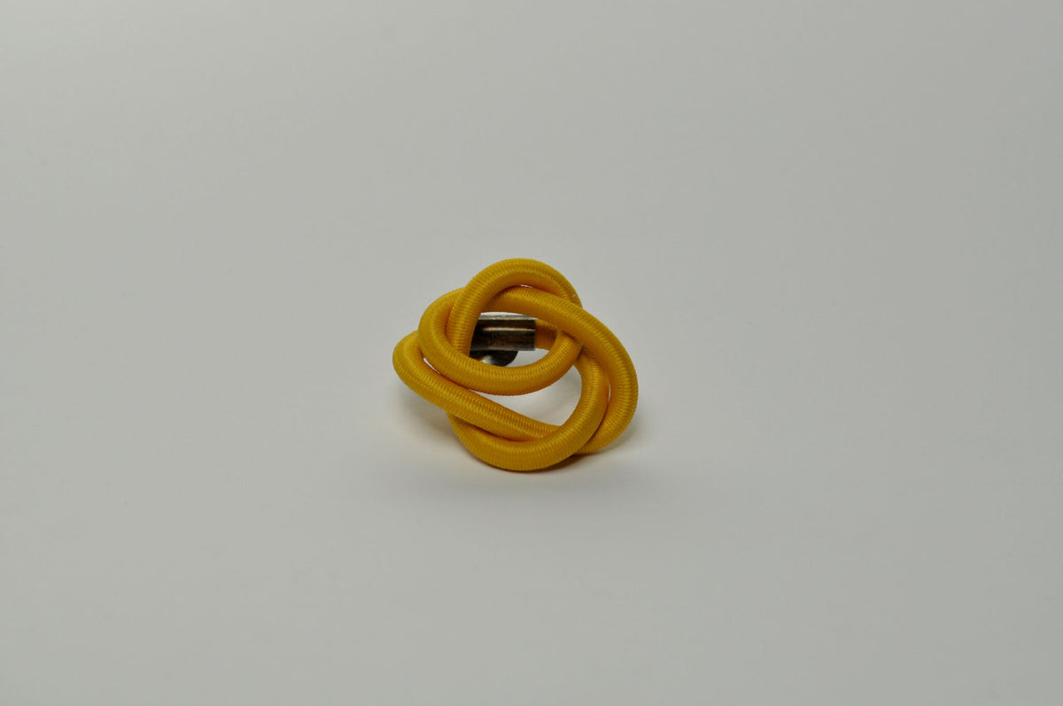 Broche entrelacée jaune, boucles torsadées formant un nœud au centre.