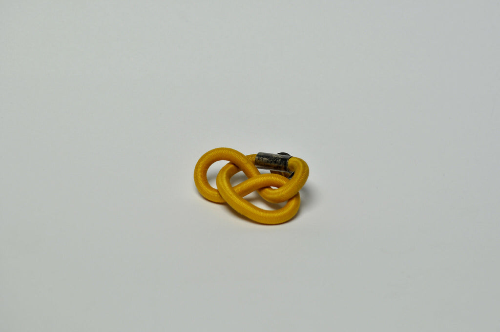 Broche entrelacée jaune, attache métallique visible à l’arrière.