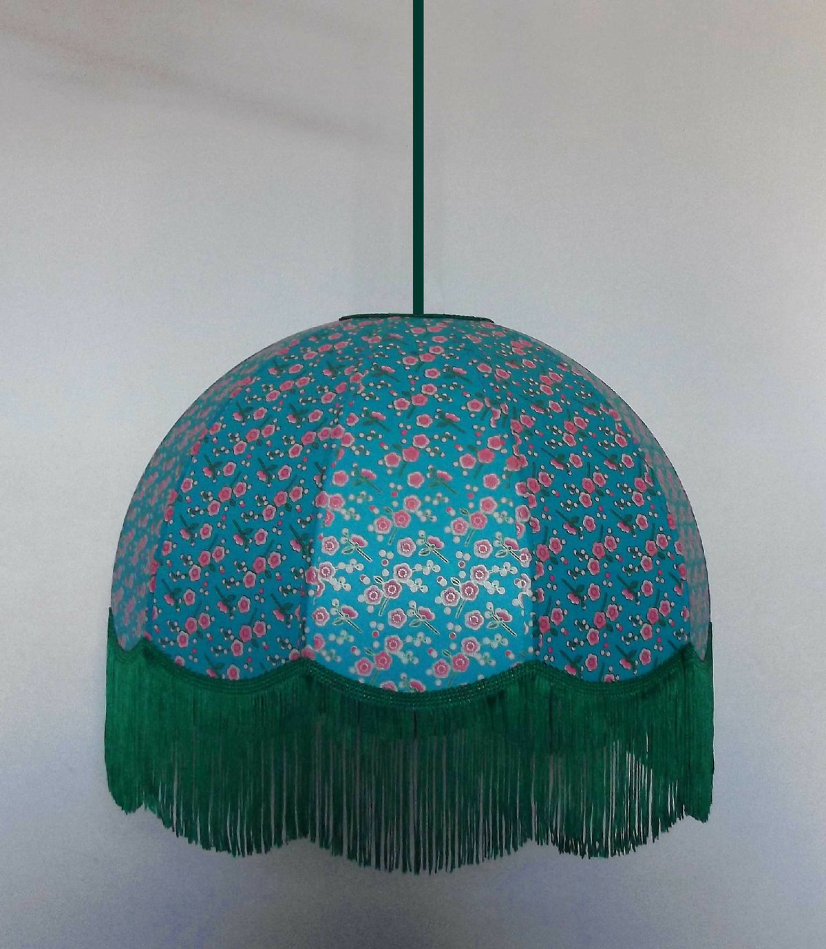 Suspension ronde en papier bleu, motifs floraux, franges vertes au bord inférieur.