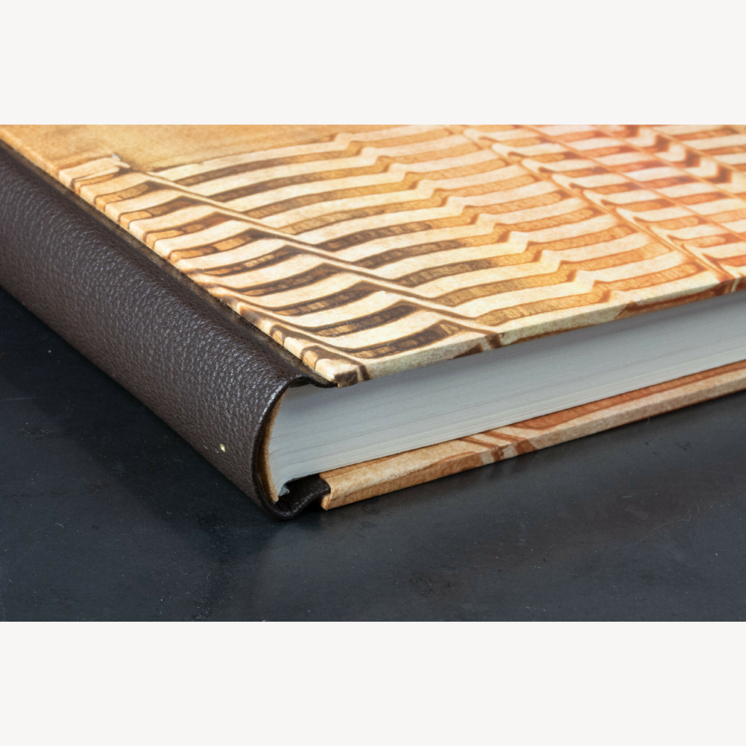 Dos en cuir brun-ocre et couverture orange à motif géométrique, tranche crème.