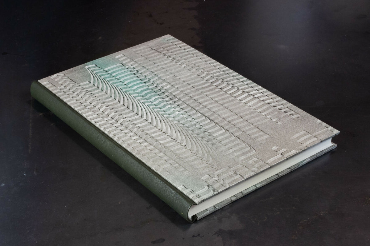 Cahier à couverture cuir gris clair à motifs en lignes, dos vert visible.