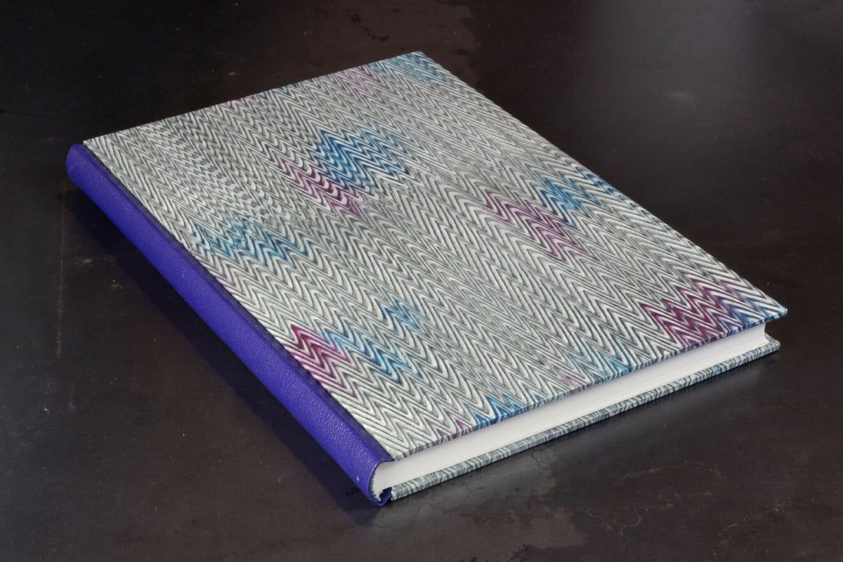 Carnet à couverture rigide grise à motif, dos en cuir violet.