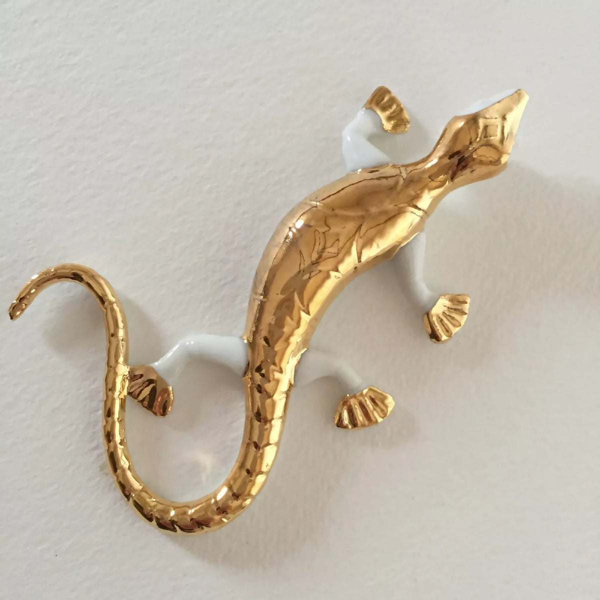 Sculpture de salamandre dorée sur fond clair, queue en boucle et détail des pattes