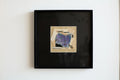 Tableau encadré noir avec collage abstrait bleu et violet sur papier clair.