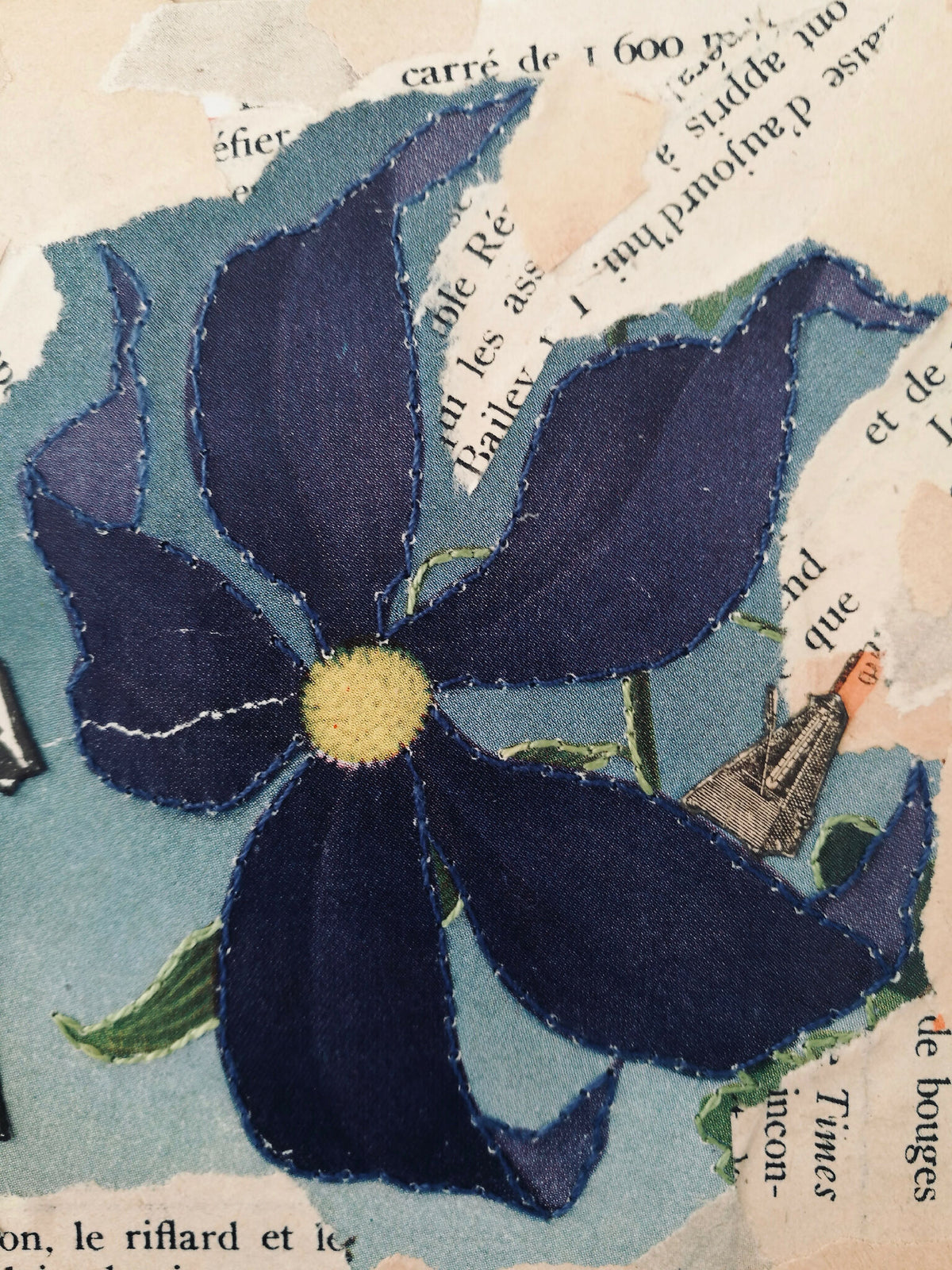 Détail de fleur bleue en collage, contours cousus et feuille verte sur papier froissé