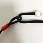 Fermoir du collier : cordon noir avec perle blanche et embout rouge