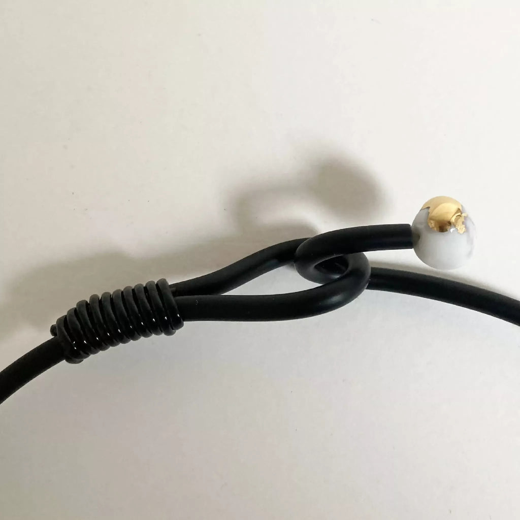 Fermoir du collier : cordon noir et attache ronde beige, détail du bracelet