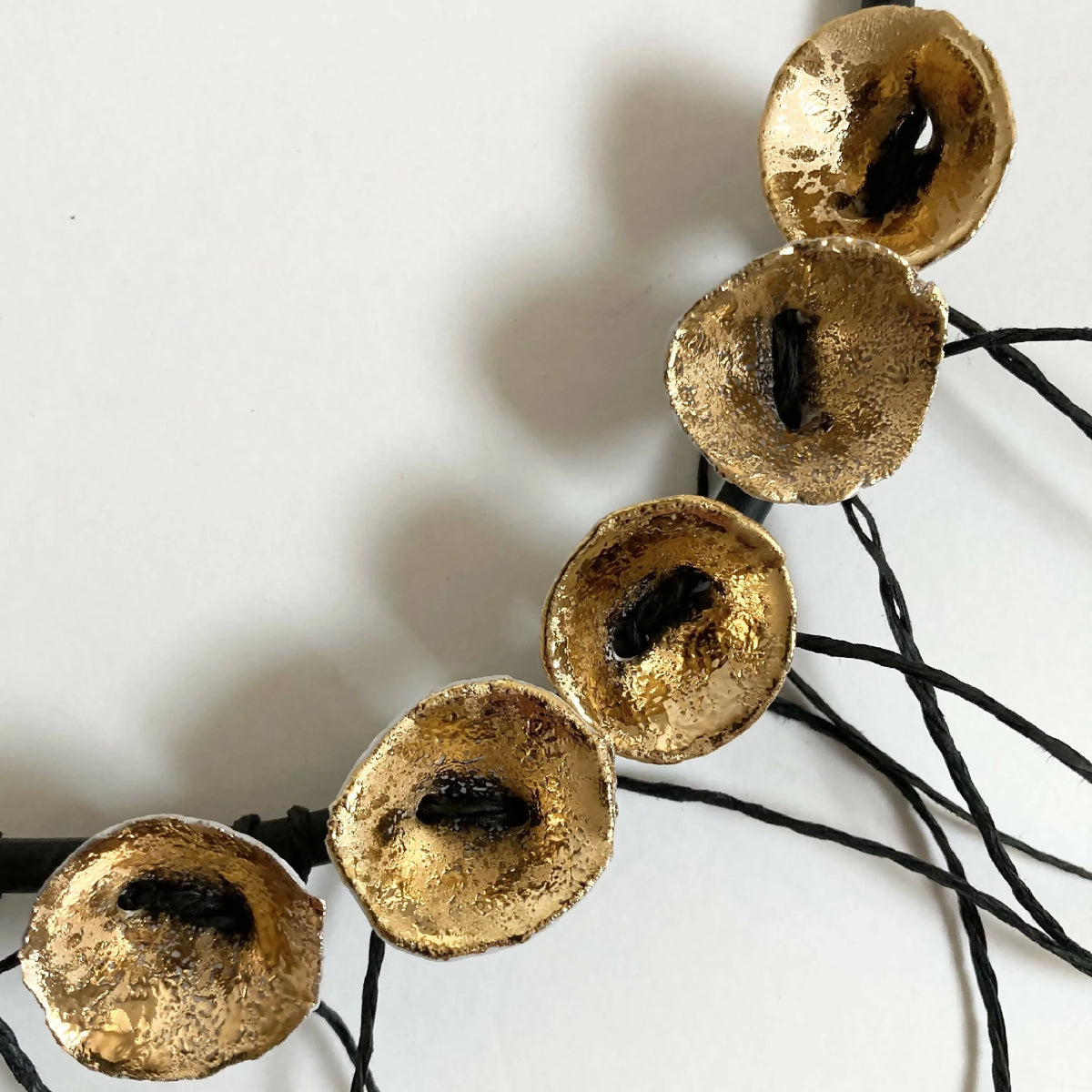 Collier : gros disques dorés percés reliés par cordons noirs, vue rapprochée