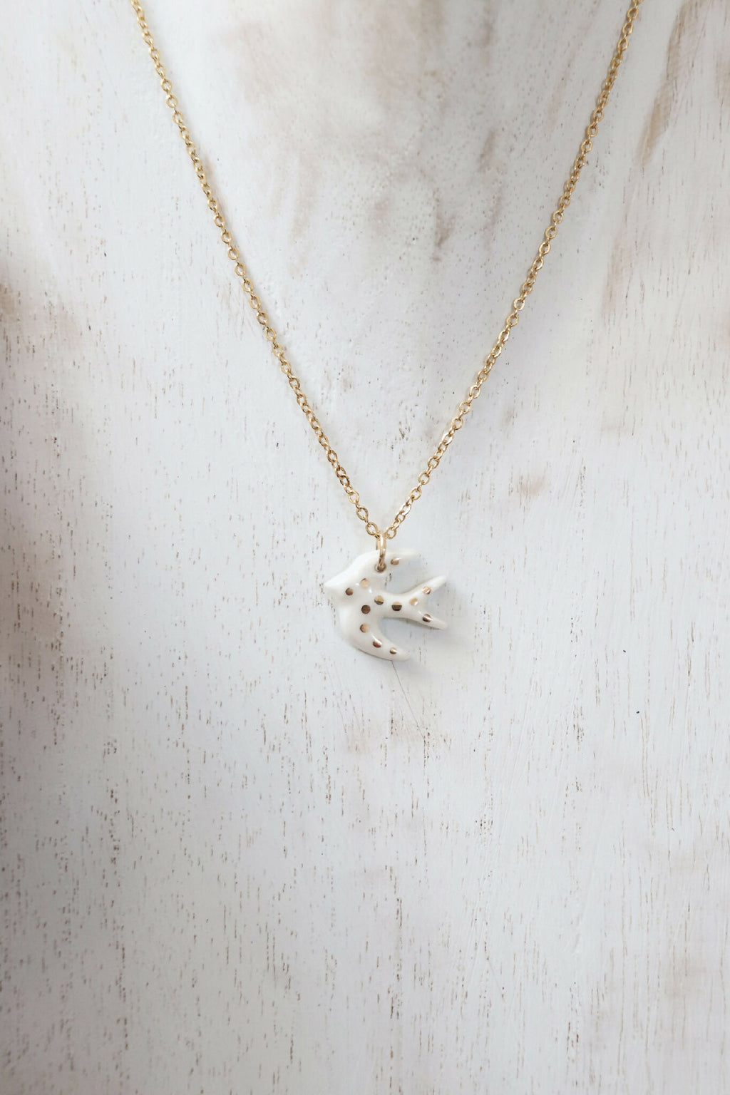 Collier à pendentif hirondelle en porcelaine blanche, chaîne dorée allongée.