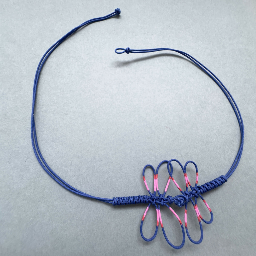 Bracelet bleu avec motif de libellule rose en frange de cordelettes, fermoir ajustable.