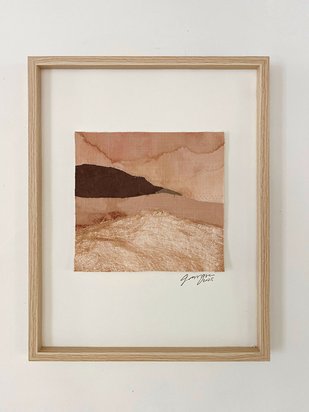 Collage textile encadré, paysage superposé beige et brun, signature en bas à droite.