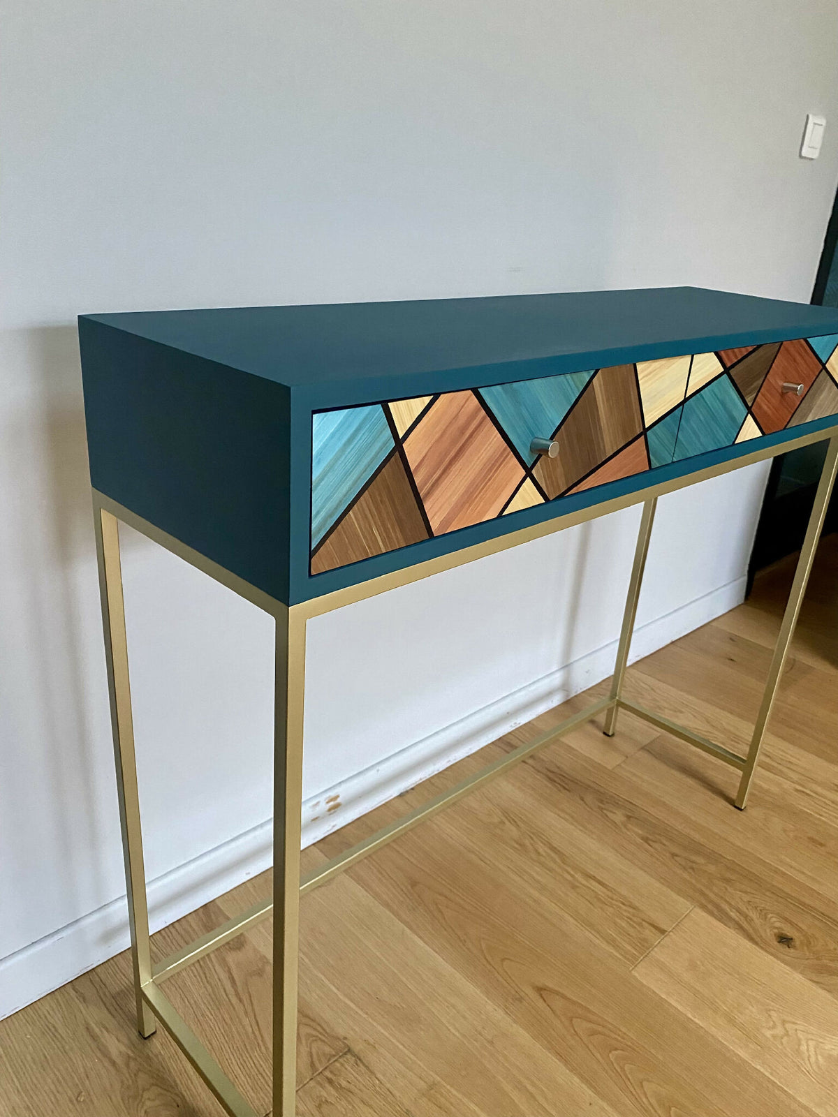 Console avec plateau bleu, structure en bois clair et tiroir à motif losanges bois et bleu.