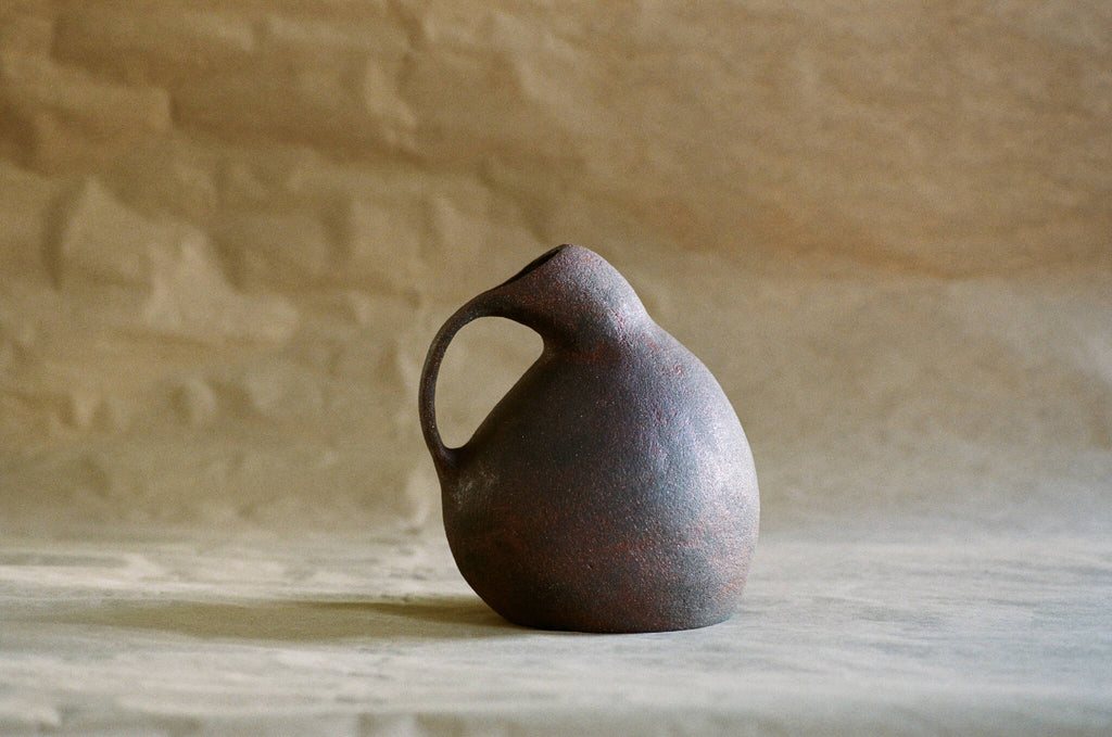 Cruche en céramique sombre, forme bulbeuse, anse latérale et bec court.