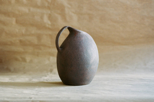 Cruche en céramique sombre, anse courbée, forme arrondie