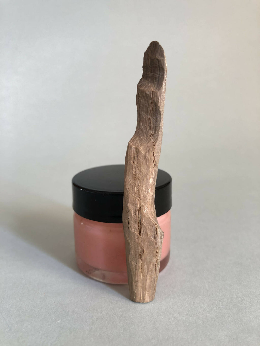 Cuillère à cosmétiques en bois, manche long, posée sur un pot à couvercle noir.