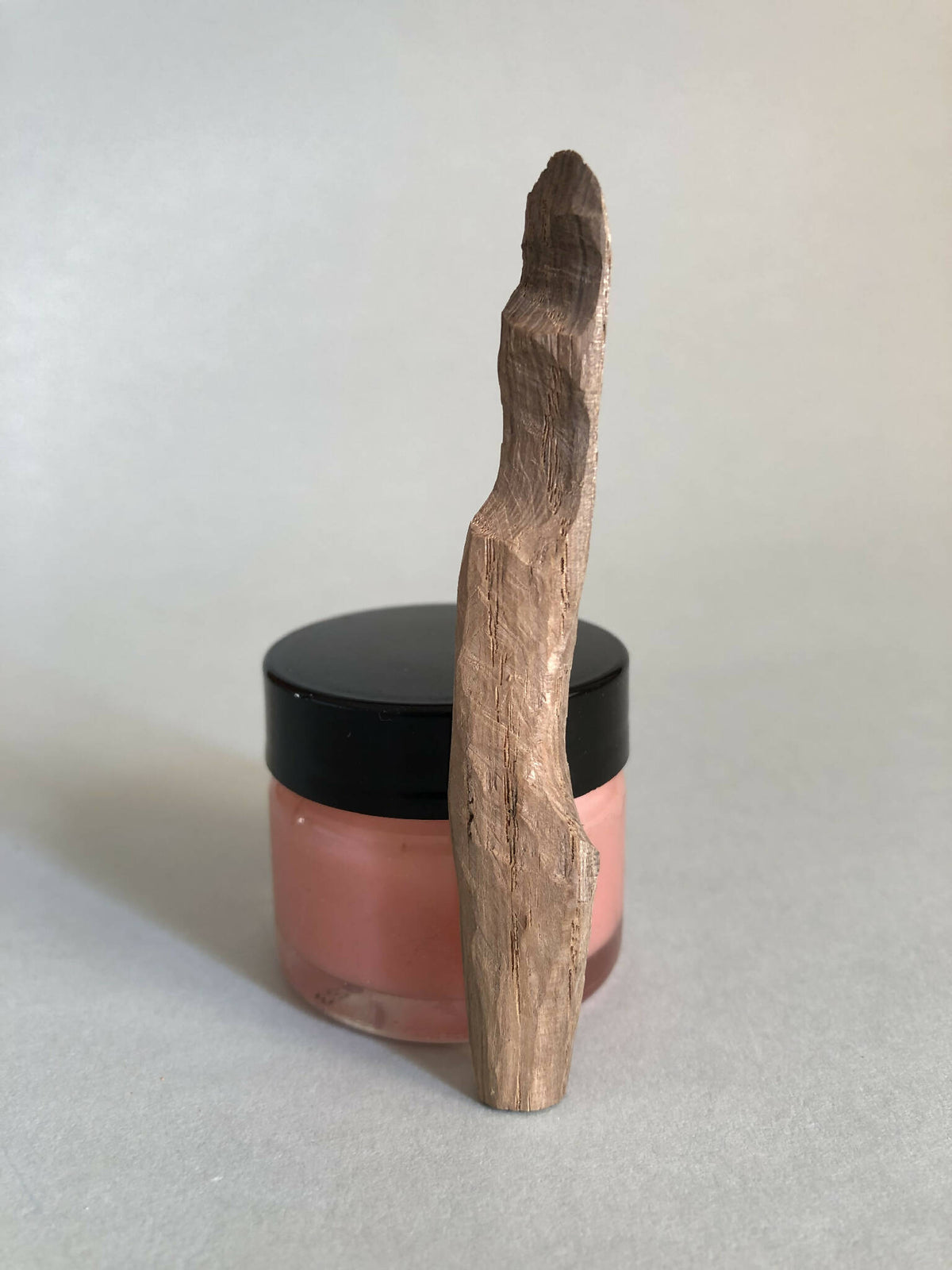 Cuillère à cosmétiques en bois, manche long, posée sur un pot à couvercle noir.